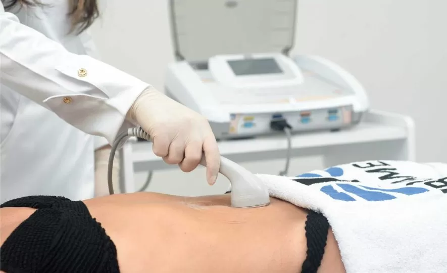 Mulher aplicando ultrassom no abdomem de uma paciente que está deitada